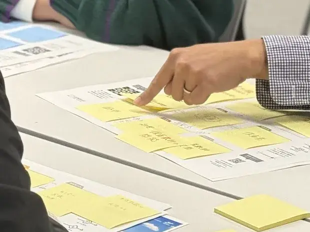 A hand pointing at sticky notes on a business diagram sheet