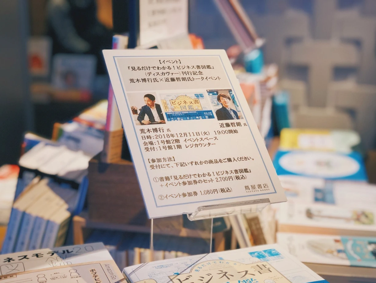 書店に立てられたイベントの案内。『見るだけでわかる!ビジネス書図鑑』刊行記念、荒木博行と近藤哲朗のトークイベント。2018年12月11日19時から、蔦屋書店。手前には『ビジネスモデル2.0図鑑』が平積みされている。