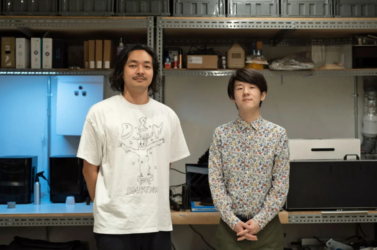 工房のような部屋に並んで立つ出村光世と近藤哲朗。