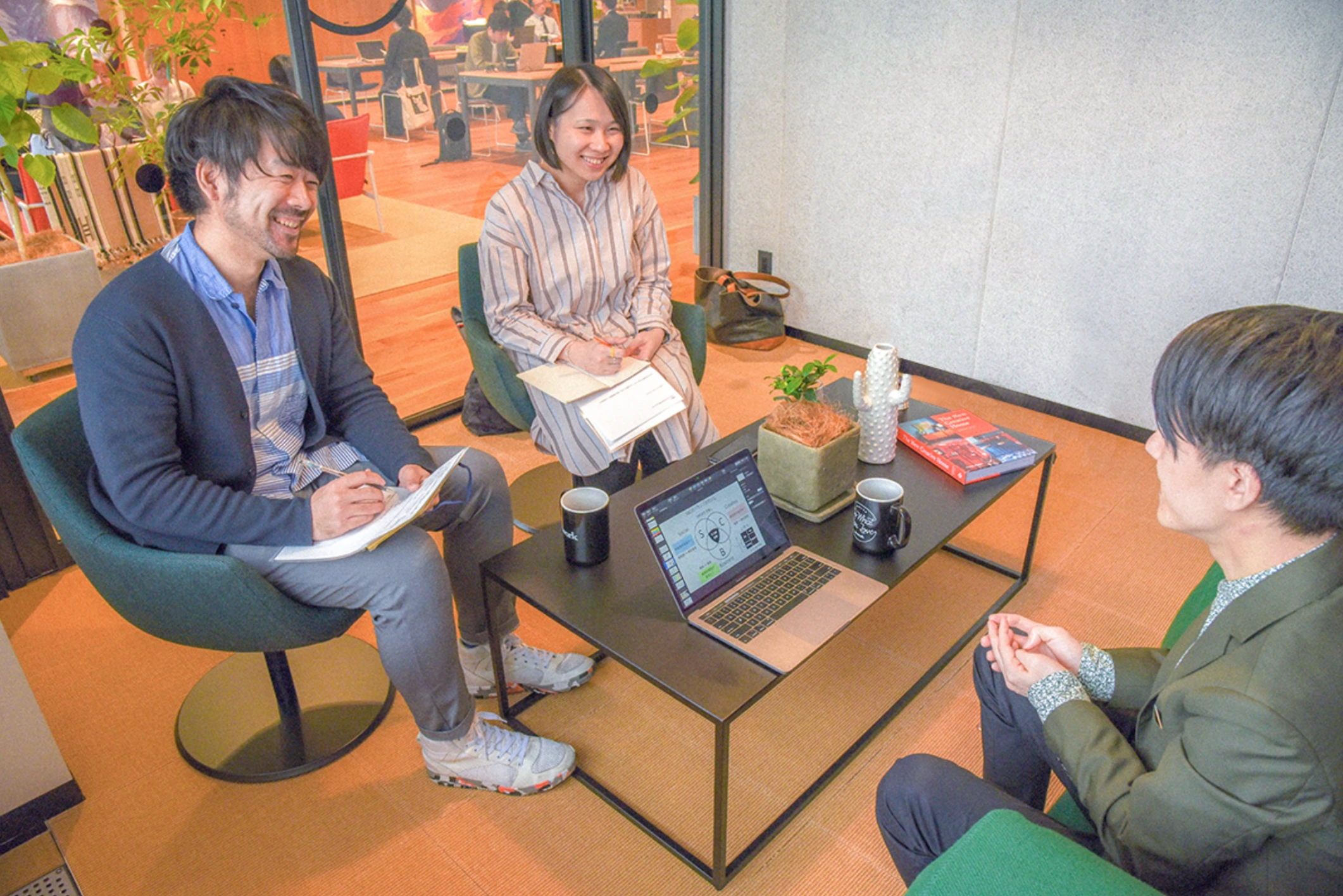 取材の様子。テーブルをはさんで3人が向かい合い、ノートパソコンにはビジネスモデル図解の画面が映っている。