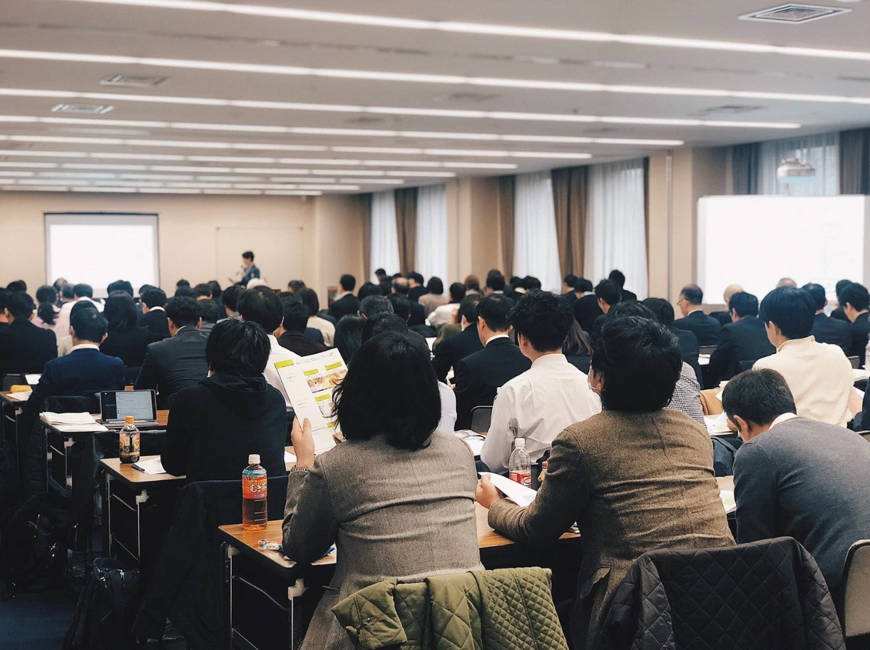 セミナー会場を後ろから写したところ。大勢の参加者が資料を手にスクリーンを見ている。